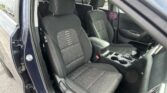 Front seats of a dark fabric car interior viewed from an open door side, showing black seats with white stitching and center console.