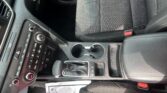 Center console area with gear shifter, cup holders, and climate controls near a fabric car seat.