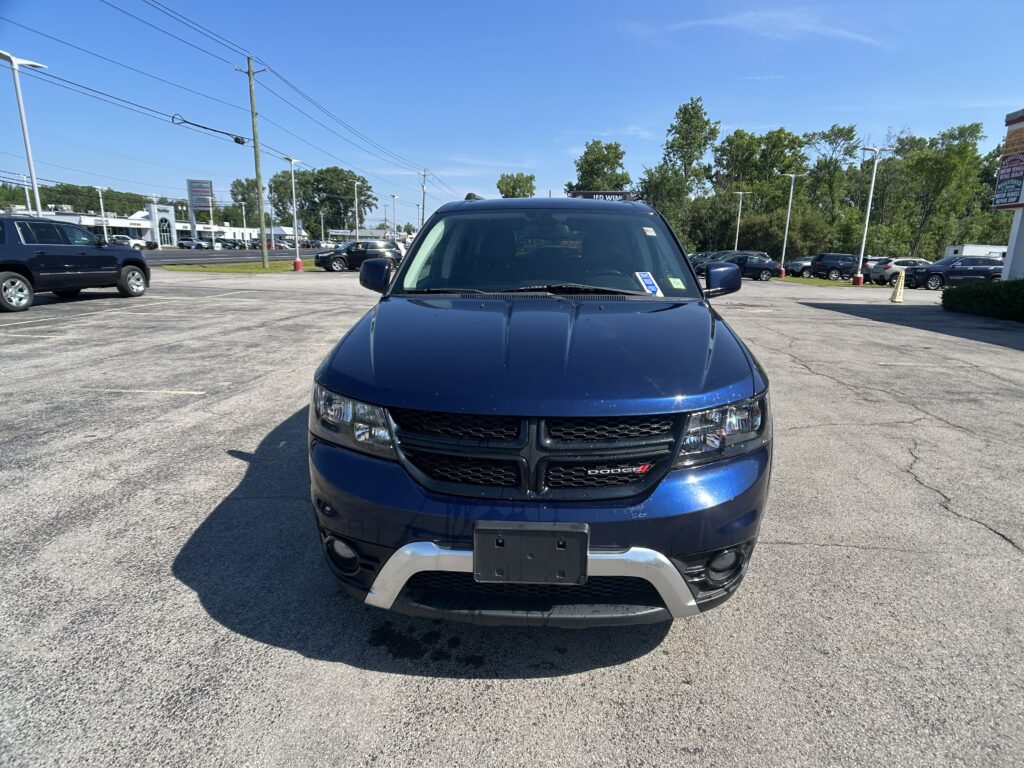 Front view of a blue Dodge SUV in a dealership parking lot on a sunny day, with other cars and trees in the background.]},{