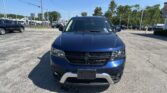 Front view of a blue Dodge SUV in a dealership parking lot on a sunny day, with other cars and trees in the background.]},{