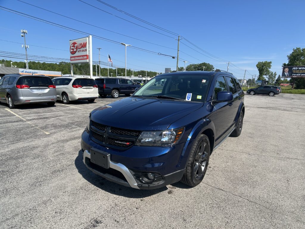Blue Dodge SUV in the foreground at a car dealership lot with other minivans parked behind under a clear blue sky.