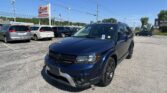 Blue Dodge SUV in the foreground at a car dealership lot with other minivans parked behind under a clear blue sky.