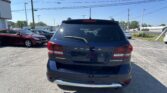 Rear view of a black Dodge Journey Crossroad SUV in a busy parking lot with other cars and power lines in the background.