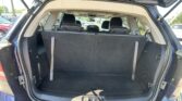 Open tailgate of a blue SUV showing an empty cargo area with the third-row seats upright and headrests visible; parking lot with other cars in the background.