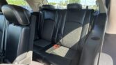 Rear car seats in black leather with headrests, visible seat belts, and sunlit rear window view of outside traffic and greenery.