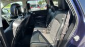 Rear passenger seating in a black leather car with headrests and visible seat belts, daylight outside through the windows (parking lot).