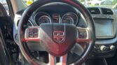 Close-up of a Dodge steering wheel with the instrument cluster and center touchscreen visible behind it in the car interior on the road outside the windshield.
