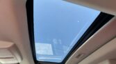 Open panoramic sunroof in a beige car, showing blue sky above.