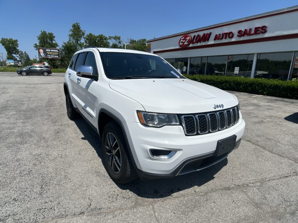 White Jeep SUV parked in front of EZ Loan Auto Sales dealership under a blue sky