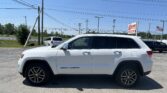 White Jeep Grand Cherokee parked in a dealership lot with an EZ LOAN Auto Sales sign and American flag in the background.