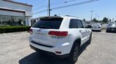White Jeep SUV parked in a dealership lot beside a white building with large windows under a clear blue sky.