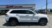 White SUV (Grand Cherokee) parked in front of E-Z Loan Auto Sales with the dealership sign and a clear blue sky in the background.