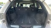 SUV cargo area with trunk open; third-row seats upright and headrests visible, black upholstery, and side panels along the load floor.