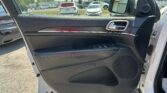 Interior view of an open car door with a black textured panel and chrome handle, looking out at a busy parking lot through the side mirror and window glass.
