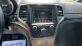 Car dashboard with a central touchscreen showing 1270 AM and climate controls, flanked by air vents; exterior parking lot visible through the windshield; a paper flyer on the passenger floor reads 'We Take Pride In Your Vehicle!'