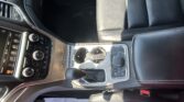 View of a car interior: center console with gear shifter, cup holders, and climate control knobs beside black leather seats