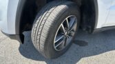 Close-up of a car's front left tire and wheel inside the wheel well of a silver SUV; visible tire tread and rim.