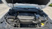 Car hood raised to reveal the engine bay of a white vehicle, with a black engine cover and visible components underneath the hood.