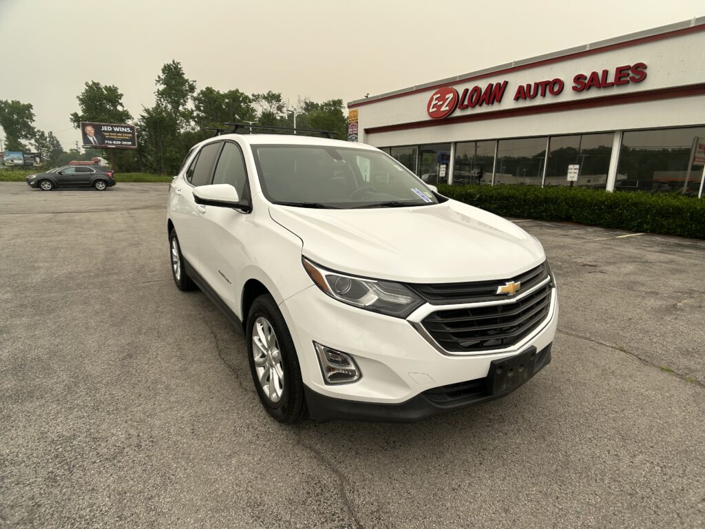 White Chevrolet SUV in a dealership lot, parked in front of an EZ Auto Sales building with red signage and large glass windows.