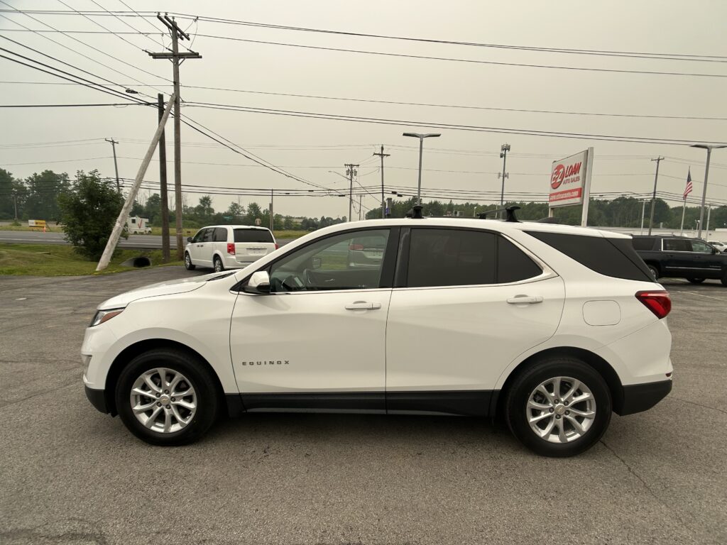 White Chevrolet Equinox parked in a car lot with a dealership sign and power lines in the background