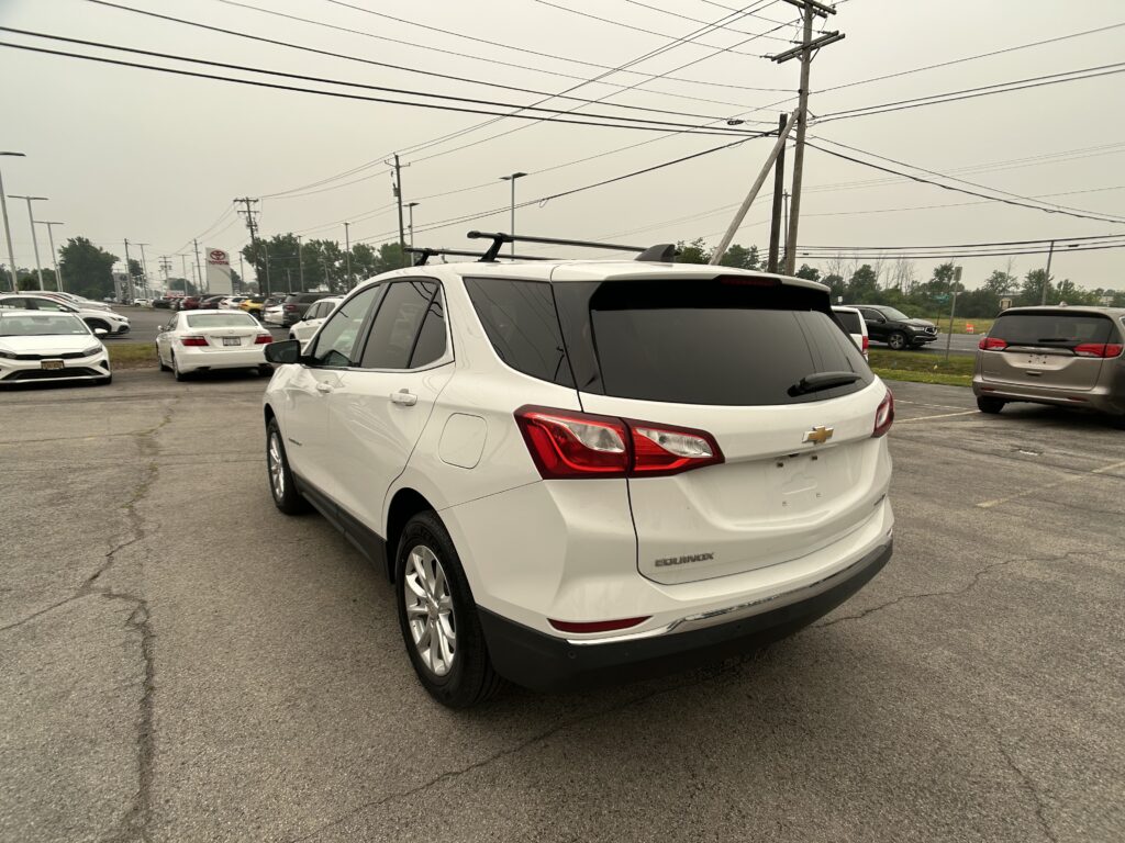 Rear three-quarter view of a white Chevrolet Equinox parked in a car dealership lot with power lines and poles overhead.