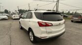Rear three-quarter view of a white Chevrolet Equinox parked in a car dealership lot with power lines and poles overhead.