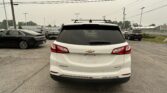 Rear view of a white Chevrolet Equinox with a roof rack in a parking lot, other cars around, overcast sky above.