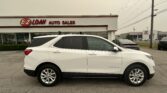 White Chevrolet Equinox parked in front of an auto dealership sign reading 'E-Z LOAN AUTO SALES' with other cars and showroom windows nearby.