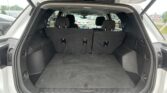 Open SUV trunk showing a spacious cargo area with third-row seats upright and a parking lot visible outside the hatch.