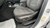 Interior of a car showing dark fabric front seats, center console with gear lever, steering wheel edge, and an open door with a warning sticker nearby.