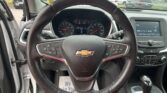 Driver's view of a Chevrolet steering wheel and dashboard, with a parking lot of cars visible through the windshield.