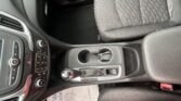 Car interior focusing on the center console: gear shift, cup holders, and climate controls next to a patterned driver seat.