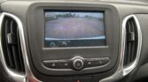 In-dash display showing a backup camera view with orange guide lines over a parking lot.