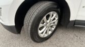 Close-up of a tire mounted on a silver alloy wheel, inside a white vehicle's wheel well on an asphalt surface.