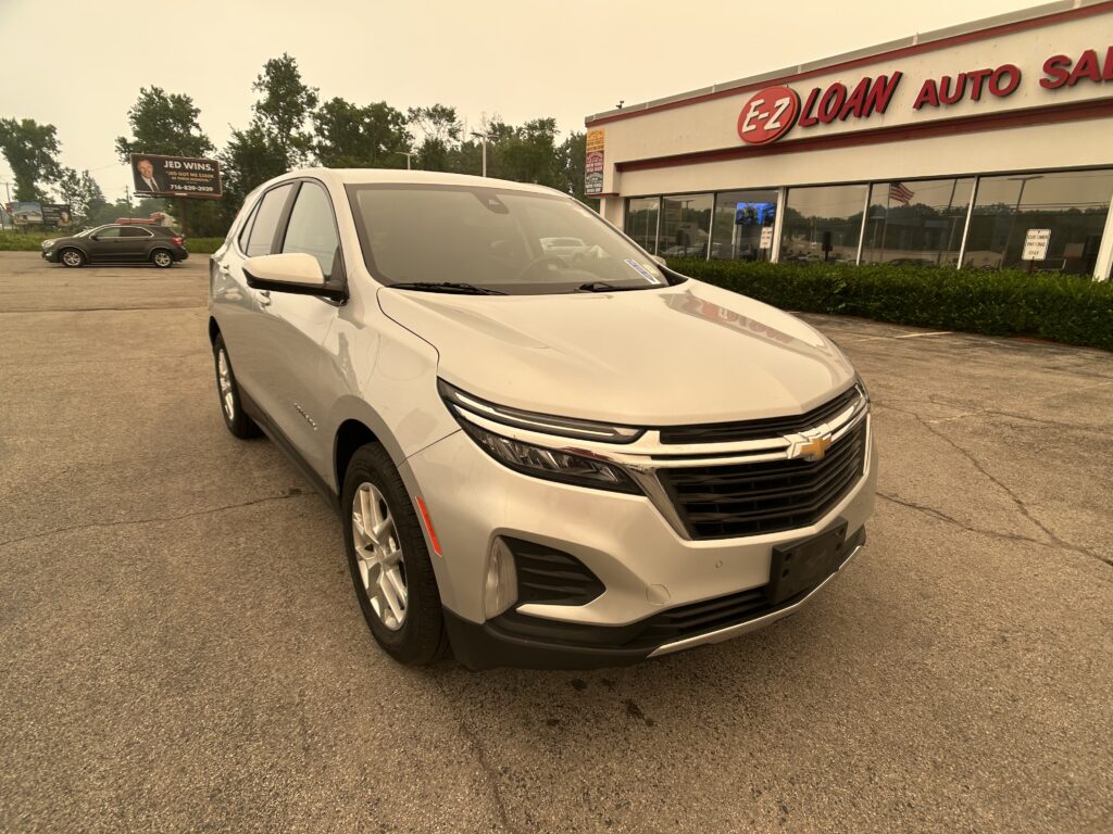 White SUV in the foreground outside EZ Loan Auto Sales dealership with a beige building and large red lettering sign in view