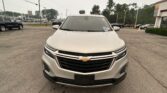 Front view of a white Chevrolet SUV in a car dealership lot with other vehicles and a building in the background]","Front close-up of the white Chevrolet SUV at a dealership, with signs and cars in the lot behind