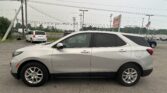 Silver Chevrolet Equinox parked in a dealership lot with power lines overhead and an American flag in the background.