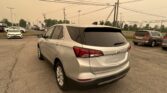 Silver Chevrolet SUV (Equinox) in a parking lot with multiple cars and power lines overhead, dealership in the background.