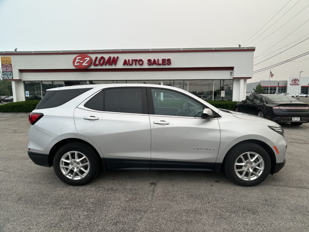 White SUV in the foreground with E-Z LOAN Auto Sales storefront in the background and a row of cars in the lot behind it.
