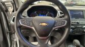 Close-up of a Chevrolet steering wheel with the instrument cluster visible behind it and a touchscreen to the right in a car interior.