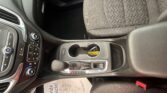 Interior of a car showing center console with gear shift, cup holders, climate controls, and patterned driver-side seat fabric