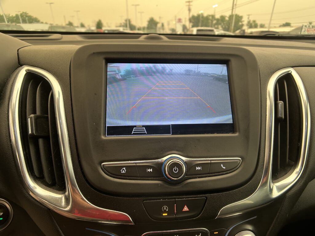 In-car display showing the rearview camera view with orange guiding lines while backing into a parking lot.