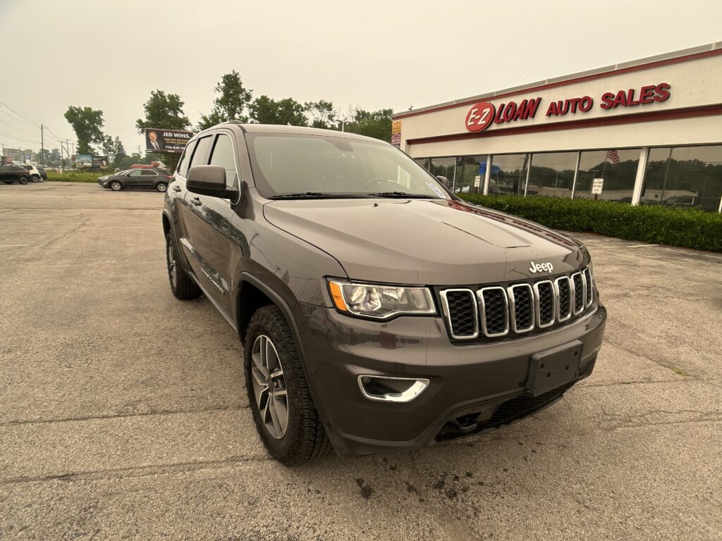 Gray Jeep SUV parked angled in the foreground outside EZ Loan Auto Sales storefront, dealership sign visible in the background