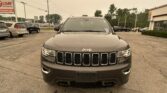 Front view of a dark gray Jeep SUV parked in a dealership lot, with other cars and a sign visible on the left.