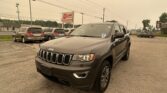 Front three-quarter view of a gray Jeep SUV parked in a lot with other minivans and a large E-Z LOAN Auto Sales sign in the background under a pale sky.