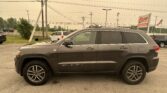 Side view of a gray Jeep Grand Cherokee in a parking lot with power lines and a roadside EZ Loan Auto Sales sign in the background.