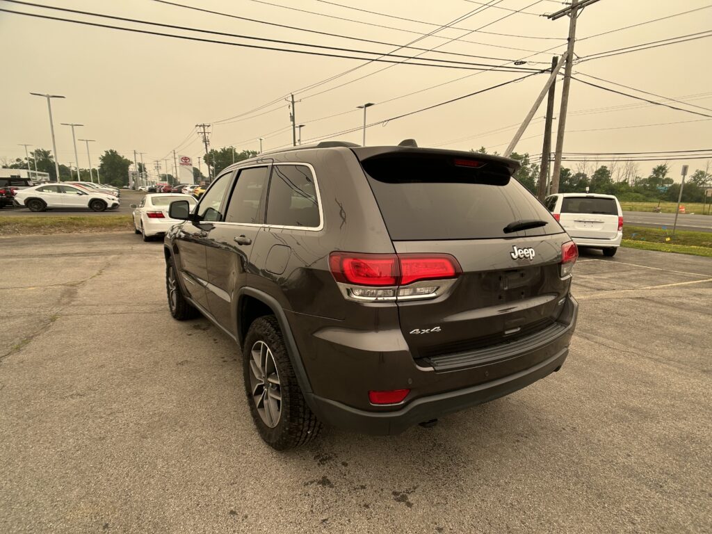 Rear view of a dark gray Jeep SUV in a parking lot, with power lines overhead and other cars in the background.