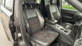 Interior of a black leather SUV with front and rear seats visible; driver's door is open and the center console with cup holders is in view.