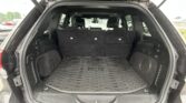 Open SUV cargo area with folded third-row seats, black interior, and rubber cargo mat; outdoor car lot visible through rear window.