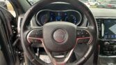 Close-up view of a Jeep steering wheel with control buttons and a digital instrument cluster behind it.